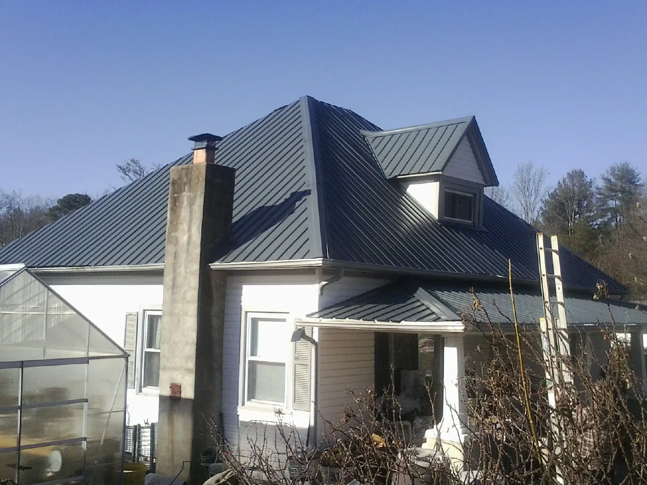 Dark blue standing seam metal roof on a white farmhouse with dormer — Slate & Tile Roof Repair by Roofing Brothers in Cosmos