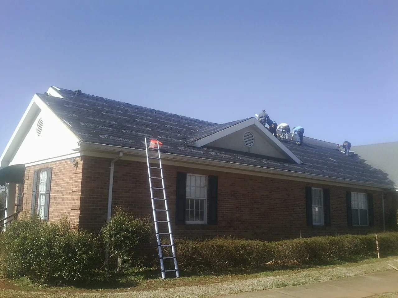 Crew tearing shingles off a brick ranch roof with a ladder set — Emergency Roof Repair work by our crew in Cosmos