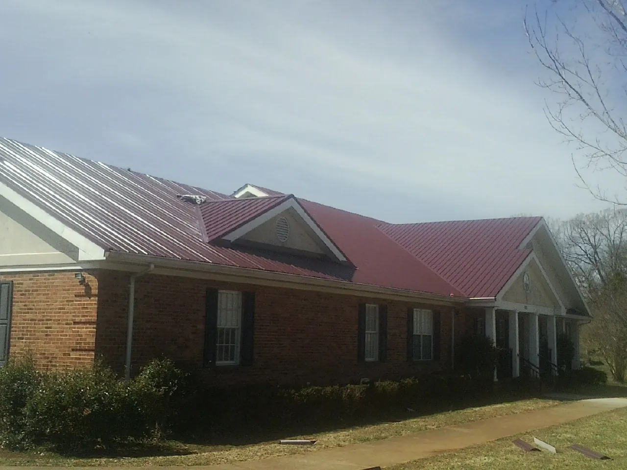 Red metal roof with gabled entries on a long brick building, from a Hail Damage Roof Repair job in Cosmos