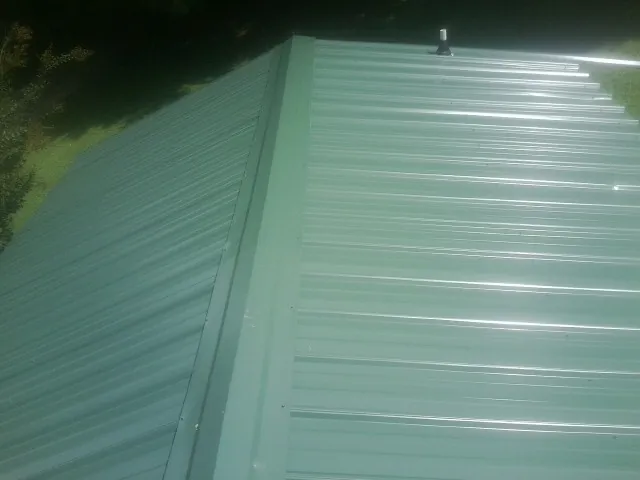 New green metal panels meeting at the ridge of a roof — Flat Roof Repair work by our crew in Cosmos