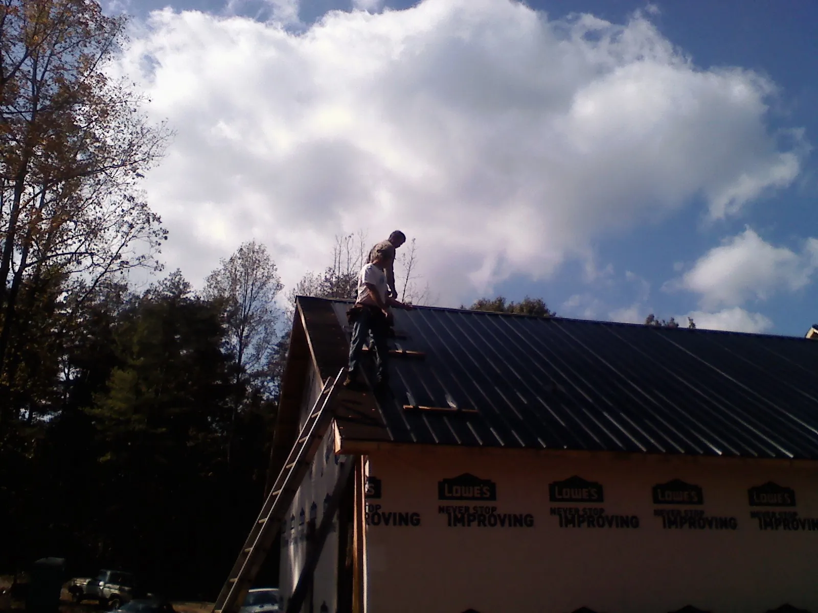 Roofer fastening dark metal panels high against a cloudy sky, from a Roof Inspection job in Cosmos