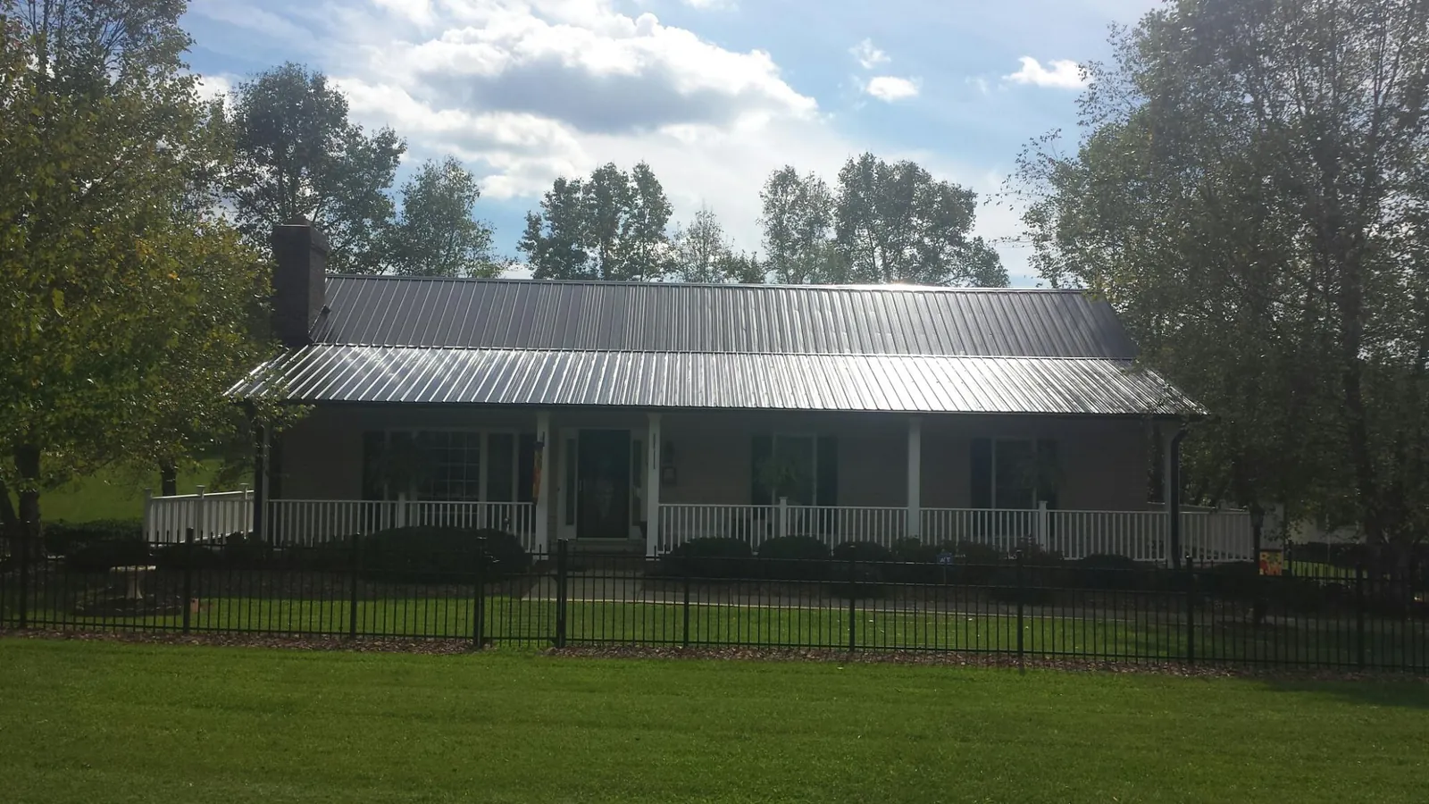 Gray metal roof on a brick ranch with a full width front porch — Gutter Guard Installation work by our crew in Cosmos