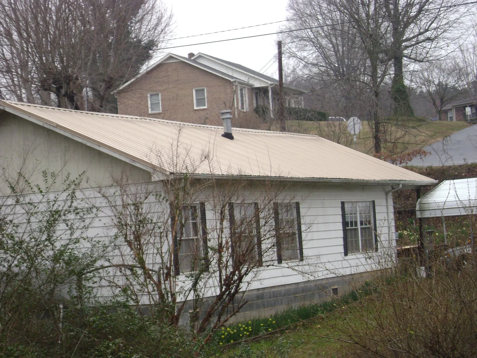 Tan metal roof on a white sided house set into a hillside — Commercial Roofing by Roofing Brothers in Cosmos