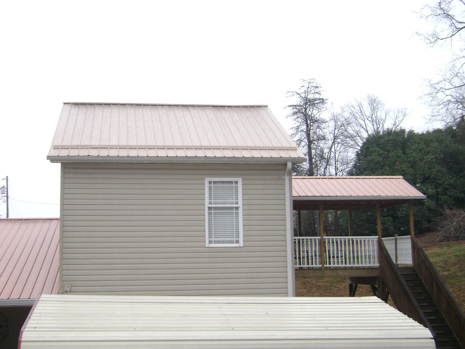 Tan metal roofs on a two story addition and attached porch, from a Roof Replacement job in Cosmos